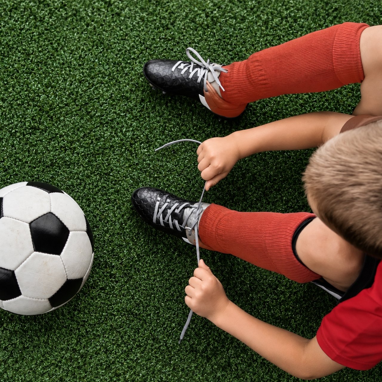 Kindergeburtstag Röthlein: Kind bindet Fußballschuhe auf dem Kunstrasen der Soccerhalle KissSoccer, 29 Minuten entfernt